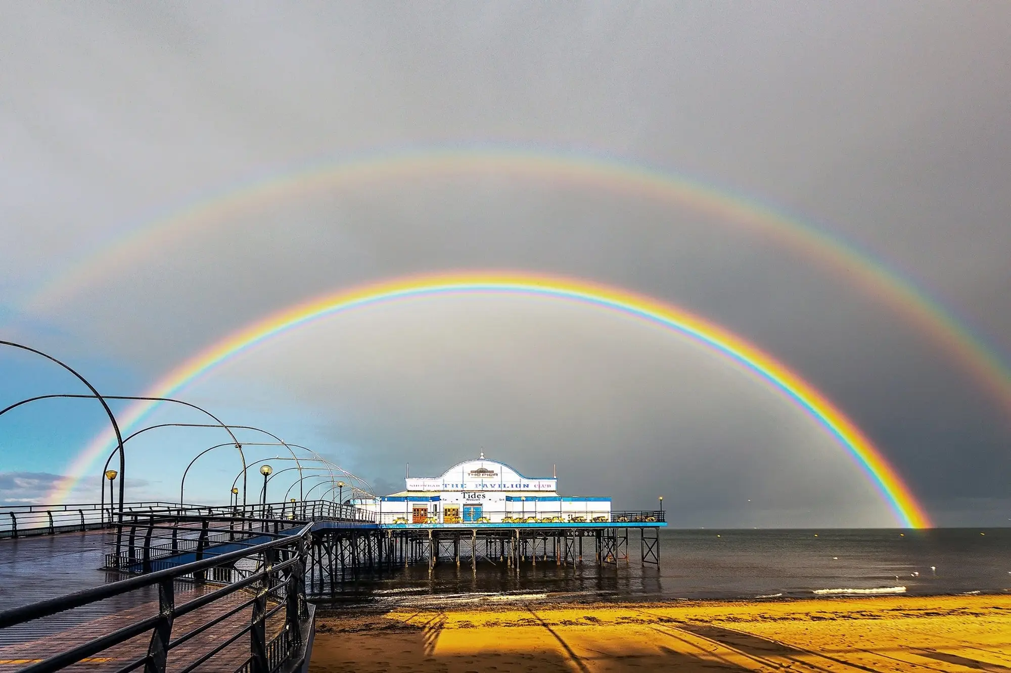 A double rainbow arching over Cleethorpes Pier and the beach after a storm
