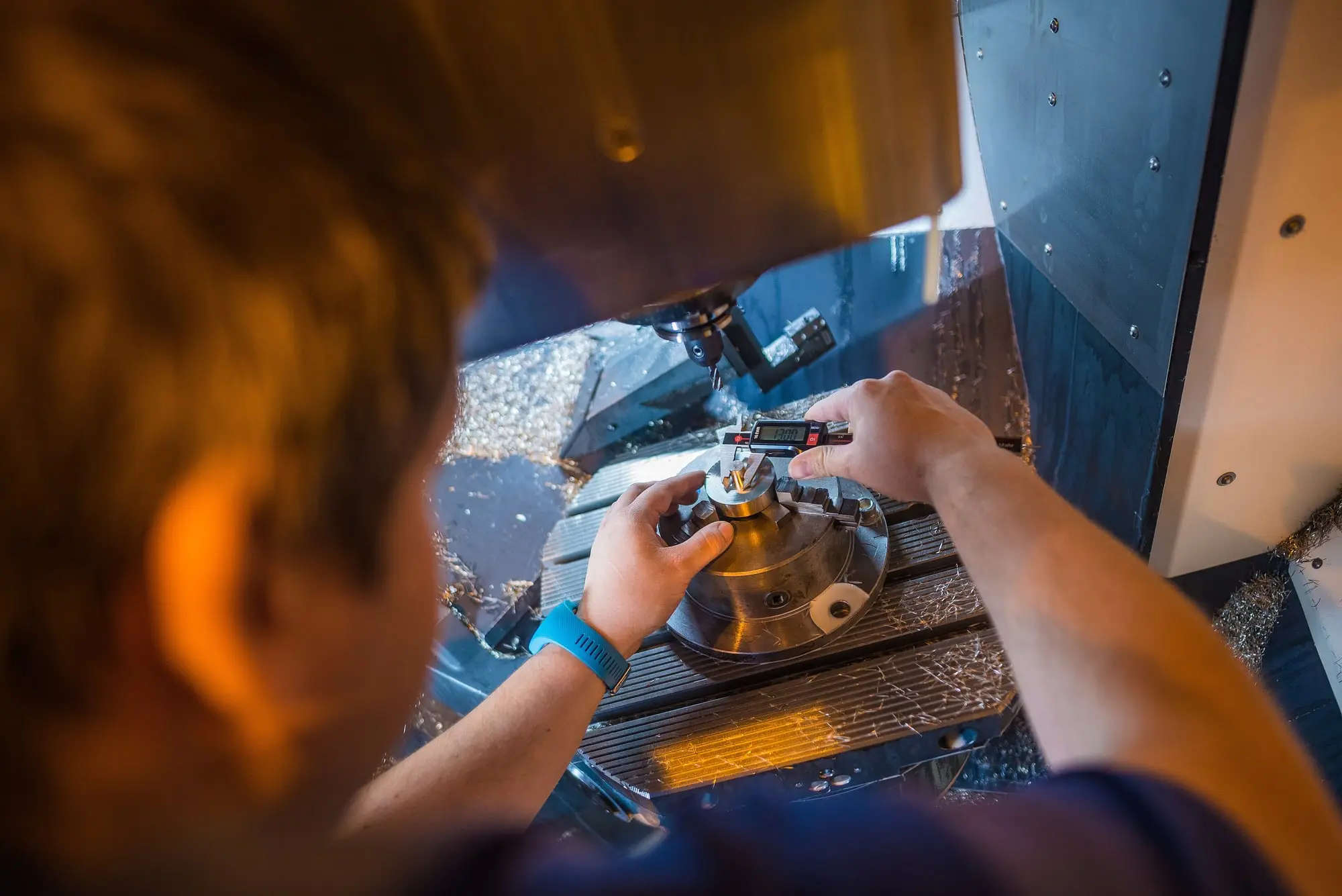 An engineer measuring a machined workpiece with a digital gauge inside a CNC machining centre