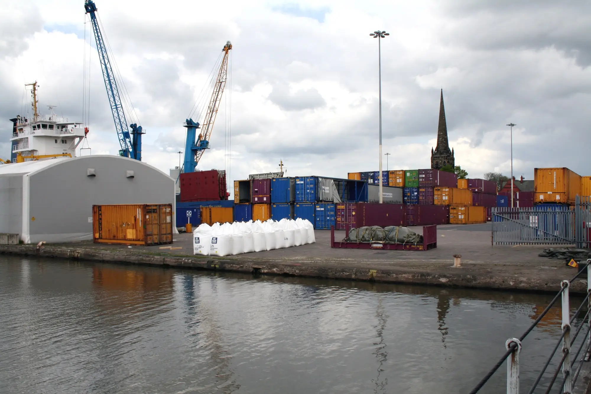 Cranes, shipping containers and a moored vessel at Aldam Dock, Goole, with the church spire in the background