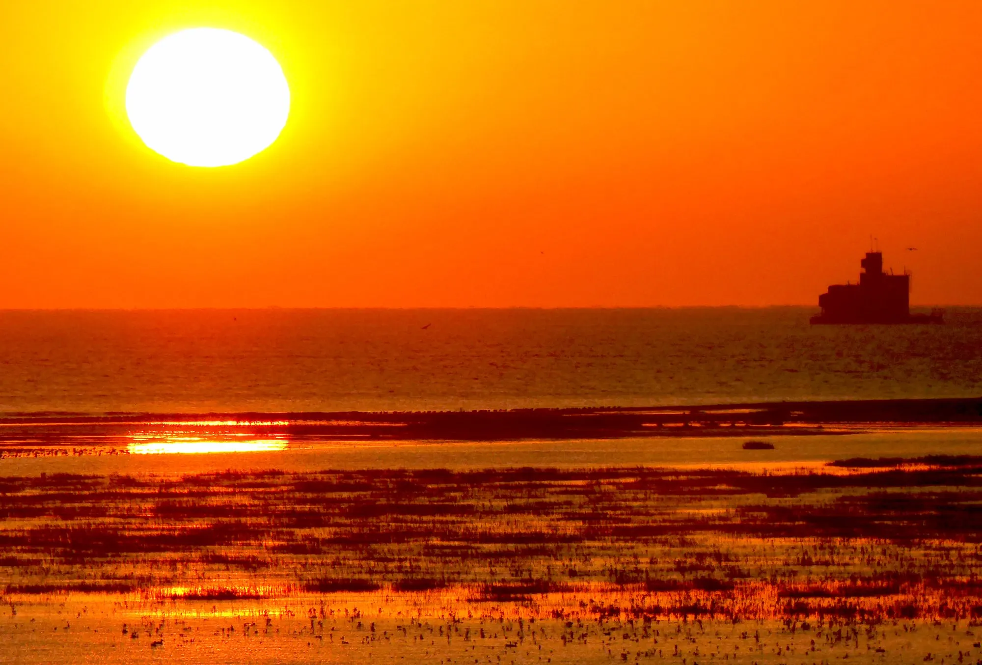 Sunrise over the Humber Estuary, the sun glowing orange above the water with the silhouette of a wartime sea fort on the horizon