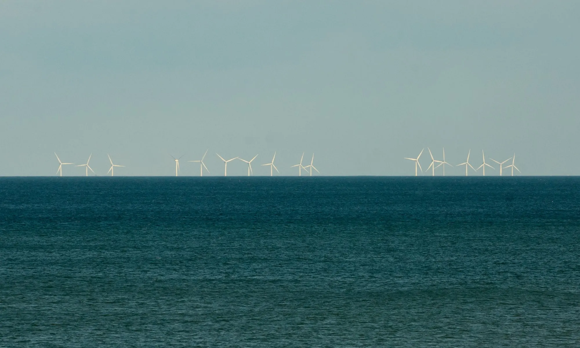 Rows of offshore wind turbines of the Westermost Rough wind farm on the North Sea horizon, seen from Barmston beach in East Yorkshire