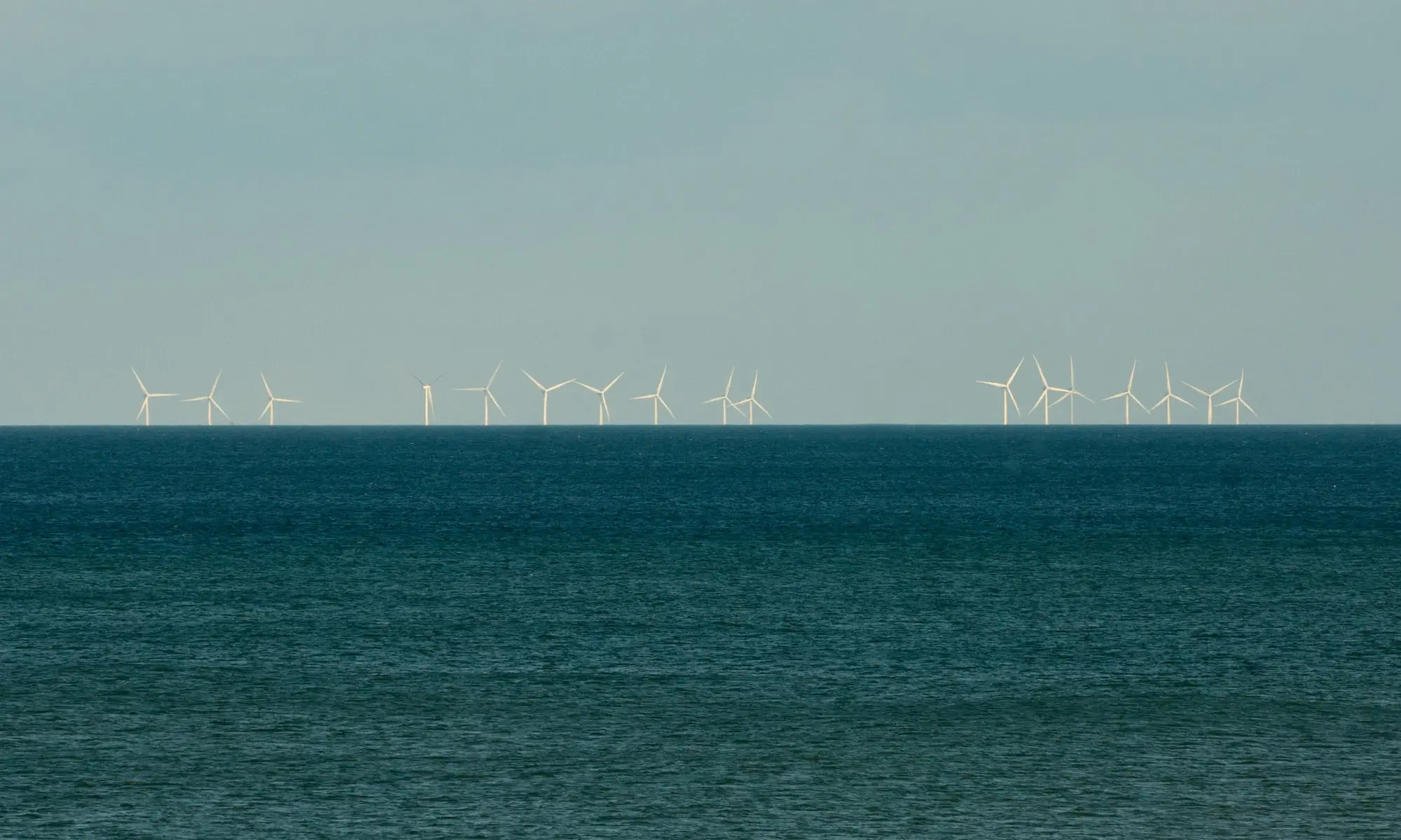 Rows of offshore wind turbines of the Westermost Rough wind farm on the North Sea horizon, seen from Barmston beach in East Yorkshire