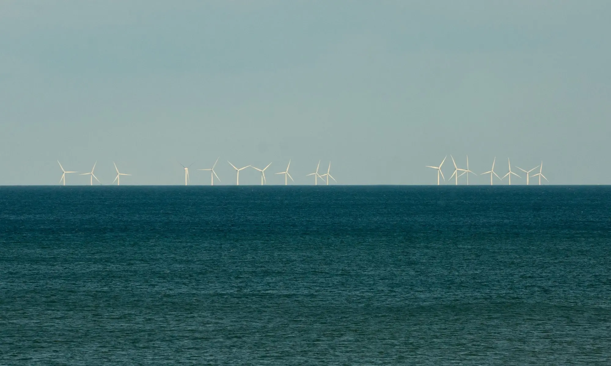 Rows of offshore wind turbines of the Westermost Rough wind farm on the North Sea horizon, seen from Barmston beach in East Yorkshire