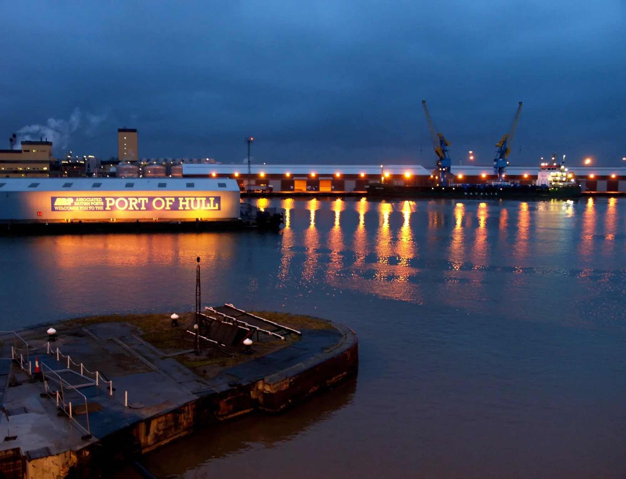 King George Dock at dusk with the illuminated 'Welcome to the Port of Hull' sign, quayside cranes and lights reflected in the water